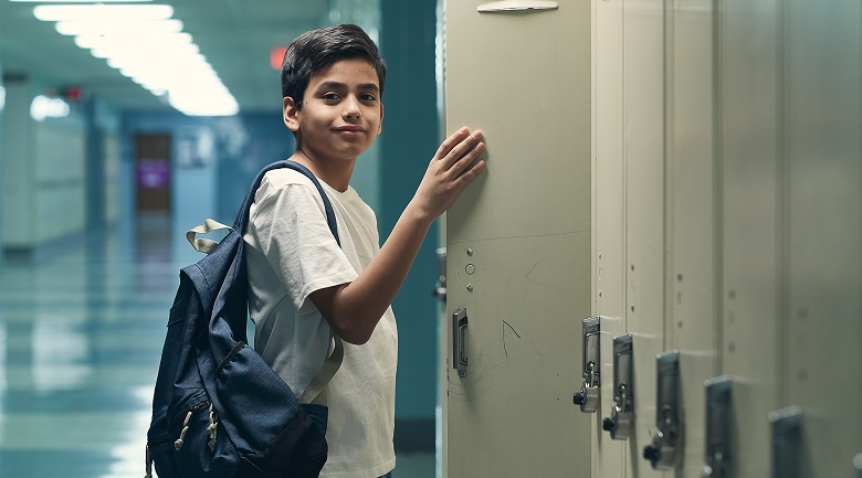 child with backpack holding locker open in hallway