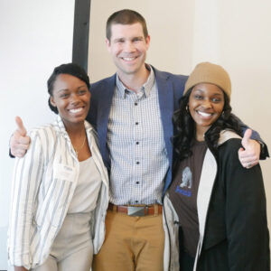 a man and two women smiling, man with thumbs up